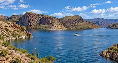 Family motorboat towing a water skier across Canyon Lake Arizona with desert canyon cliffs in the background
