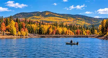 Angler fishing from a small aluminum boat on Fool Hollow Lake surrounded by colorful autumn foliage in the Arizona White Mountains