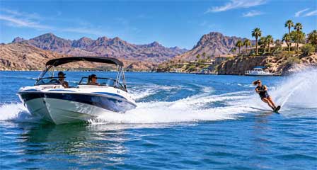 Motorboat towing a female water skier across Lake Havasu with waterfront homes and desert mountains