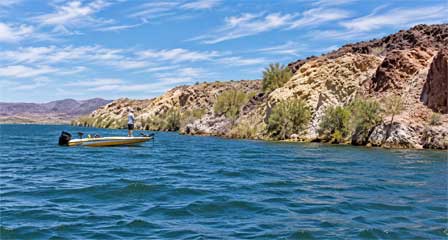 Bass fisherman casting along the rocky shore of Lake Mead surrounded by rocky mountains and desert scenery