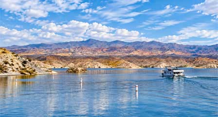 Houseboat heading up lake on Lake Mead surrounded by colorful mountains and desert