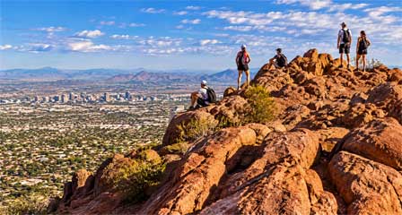 Five hikers on the rocky summit of Camelback Mountain overlooking downtown Phoenix and the surrounding city