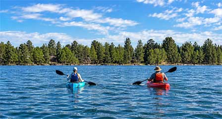 Two kayakers paddling across Rainbow Lake near Pinetop-Lakeside Arizona with pine-covered shoreline and lakeside homes