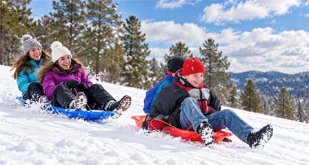 Kids sledding down a snow-covered hill with pine trees in Arizona snow country